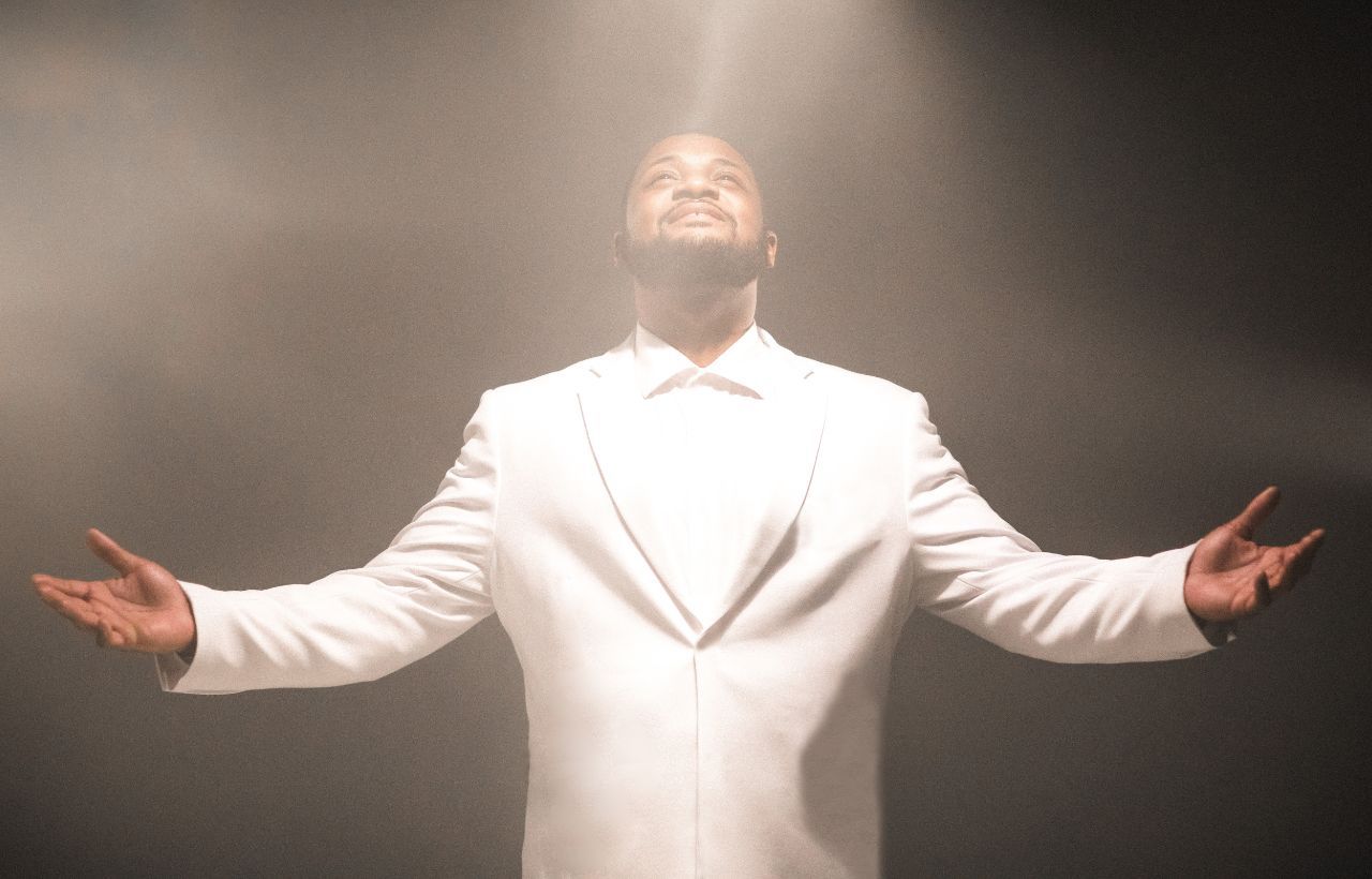 A man in a white suit holds his hands outstretched as he raises his head to the sky.