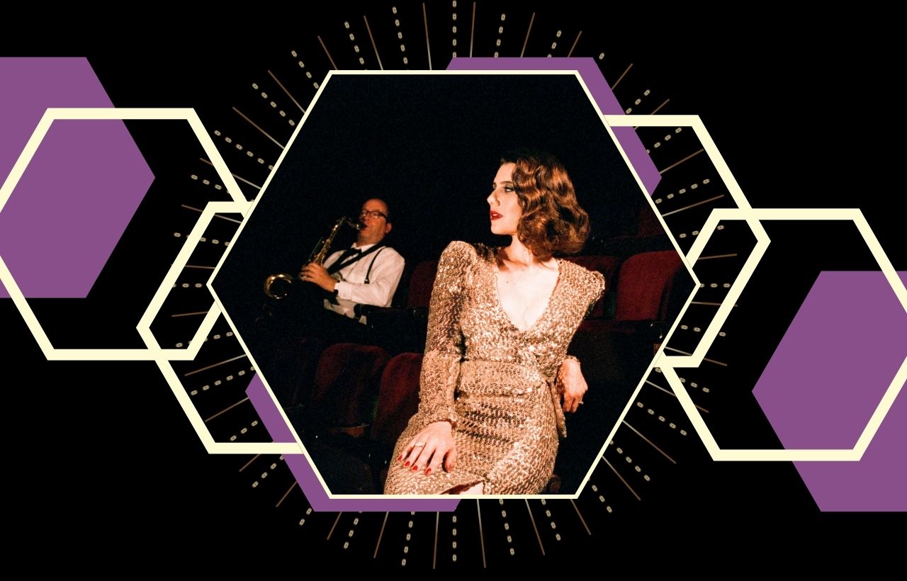 A person in a sequined outfit sits in a theater seat while another person in the background plays a saxophone, all framed by geometric hexagon designs.