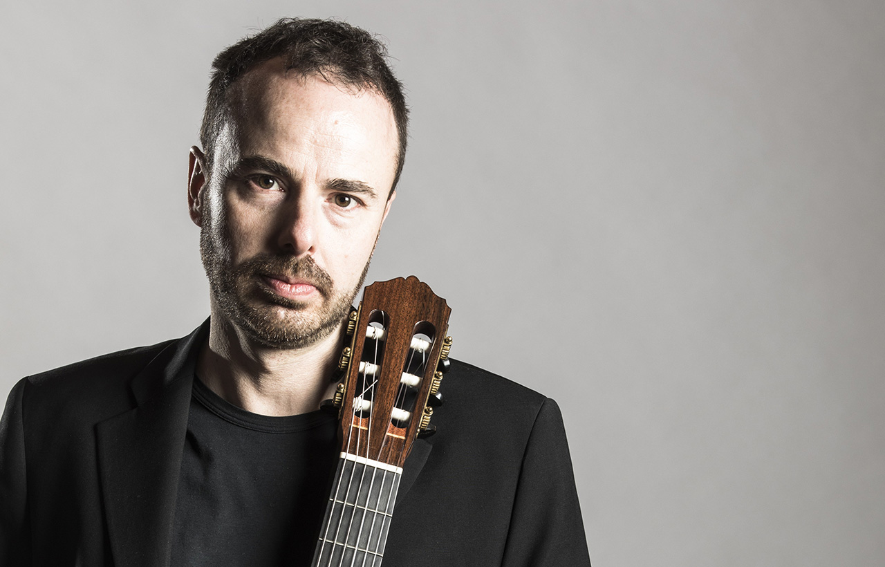 Lorenzo Micheli holding a guitar against a gray background