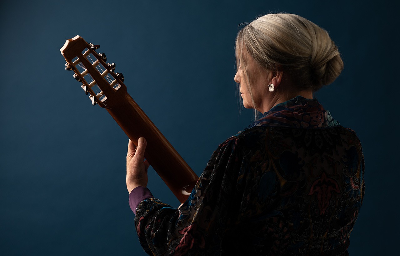 Raphaella Smits holding a guitar against a blue background, with her back to the camera