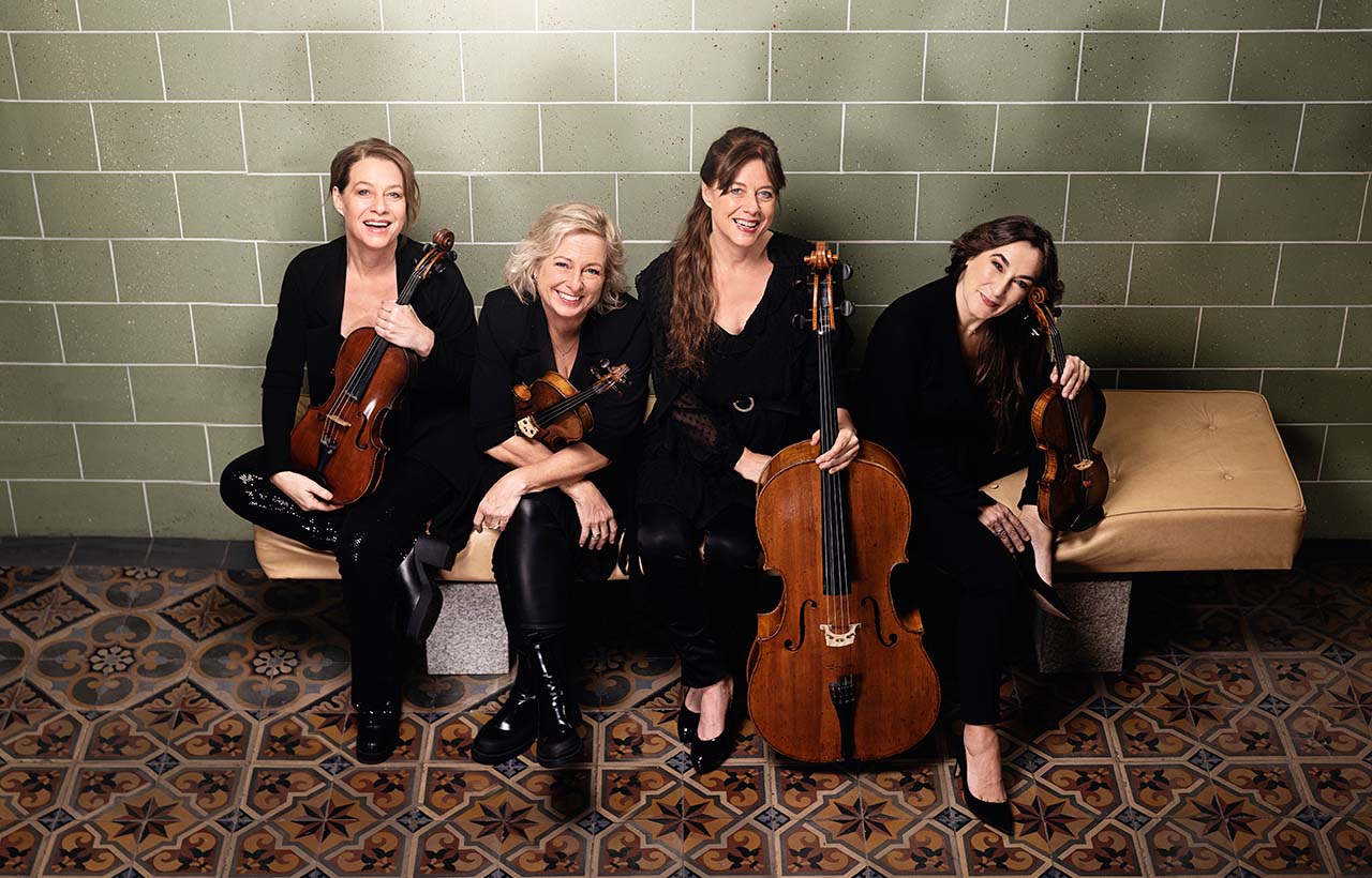 Members of the Vertavo String Quartet seated on a tan bench in front of a green tiled background